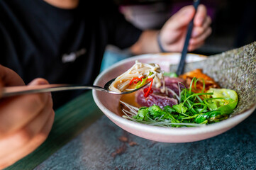 Close-up of a vibrant bowl of noodle soup with fresh vegetables and a spoon, perfect for culinary themes. The image highlights the appeal of healthy and appetizing food.
