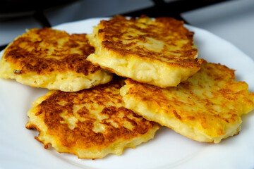 Cooked fried fresh potatoes pancakes, draniki on plate on kitchen at home. Preparing fresh dish. Cuisine, culinary, recipe. Traditional Russian food on lunch dinner fry on vegetable oil.