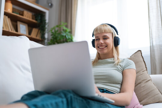 Young happy freelance worker or university student woman sitting work at home on sofa working on laptop, while listening podcast or listen the music, favorite song, enjoying freedom and independence.