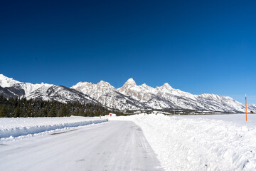 Obraz premium A sunny view of the Teton Mountain Range covered in snow during a cold winter.