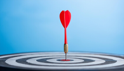 Arrow at darts target, pastel blue backdrop. Business and achieving goals concept.