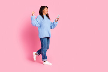 Full body portrait of nice young girl ralk use phone raise fist empty space isolated on pink color background