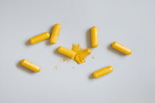 Opened Medical capsules to show yellow powder on grey top view. Taking dietary supplements