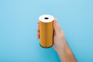 Young man hand holding and showing car new oil filter on light blue background. Pastel color. Closeup. Front view.