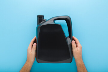 Young man hands holding and showing 5L dark black plastic container for car motor oil on pastel blue table background. Closeup. Empty place for text or logo on can. Point of view shot. Top down view.