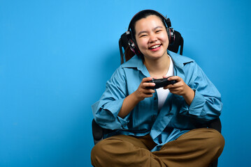 Happy Young Asian woman play game controller video console playing holding hobby playful Online Video Game enjoyment eSport Cyber Games Internet isolated on blue backround © Andri