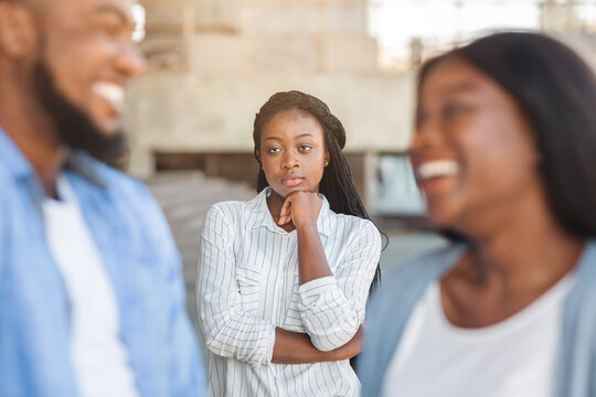 Upset black woman watching her ex boyfriend happy in relations with new girlfriend, looking jealous on background, selective focus