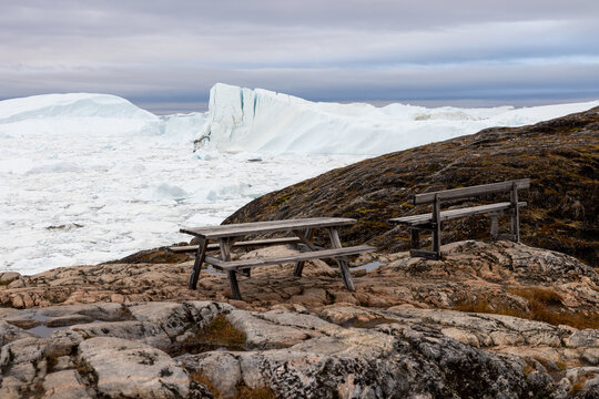 Wooden bench and a table on top of the hill outdoors with spectacular views at white giant icebergs in Ilulissat Icefjord in Greenland
