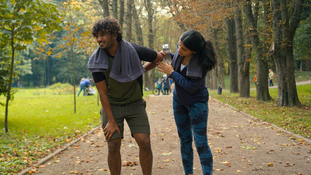 Outdoors in nature park Indian Arabian couple friends man woman stop after cardio fast run jog running man tired exhausted resting feel bad unwell pain ache girl calm support care of guy people sports