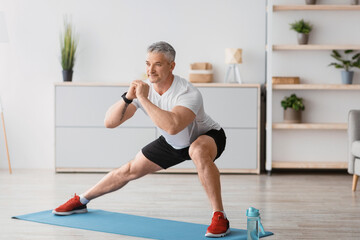 Home serobics. Mature man doing lunges exercises on mat in living room, enjoying domestic fitness...