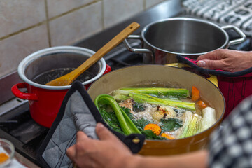 Cooking - womans hands preparing chicken stock broth or bouillon with vegetables in a pot. Kitchen - scenery from abov