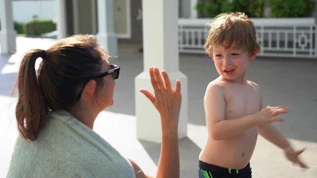 Mother applying sunblock protection cream to her son by pool in summer and giving a high five