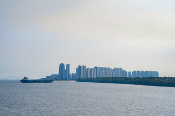 Naklejka premium Tuas Second Link Bridge connecting Singapore and Johor, Malaysia. Buildings at Forest City and Singapore's port. View from the Straits of Johor.