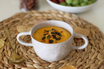 Pumpkin and potato creamy soup, bowl of grapes, jars of nuts and autumn leaves on the table. Selective focus.