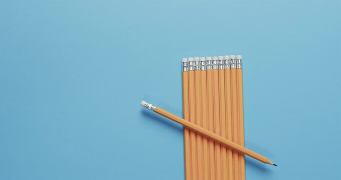 A single yellow pencil lies across a neat row of pencils on a blue background