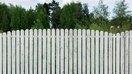 Fototapeta premium White wooden fence on the green summer garden forest background. front view