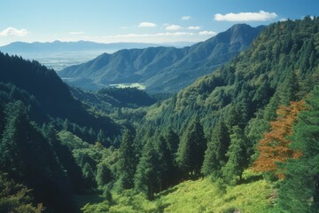 Obraz premium a breathtaking view of a mountainous landscape. The sky is blue with some clouds, and the mountains are covered with lush green trees.