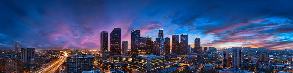 Fototapeta premium Modern cityscape of Los Angeles City with skyscrapers and highways, Los Angeles river in the background at dusk, illuminated by street lights. A Vincent Thomas bridge connecting two parts of downtown