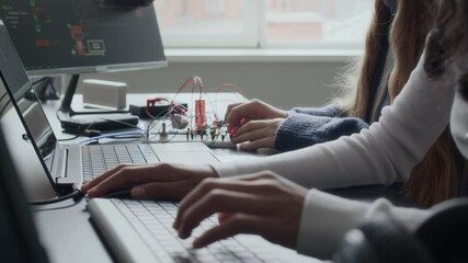 Cropped shot of two diverse gen z female school students using computer while working on electronics project in classroom, connecting wires to circuit board and entering code on keyboard - Powered by Adobe