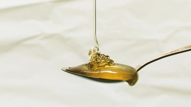 4k Reverse shot of honey dripping on a metal spoon.