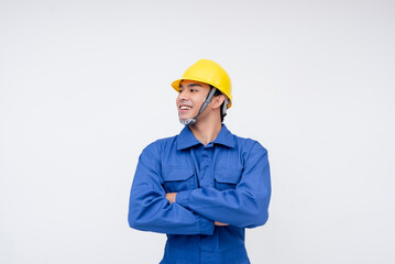 A confident asian construction worker stands with arms crossed looking to his left, wearing a blue uniform and yellow hard hat. Skilled labor, and industrial professions.