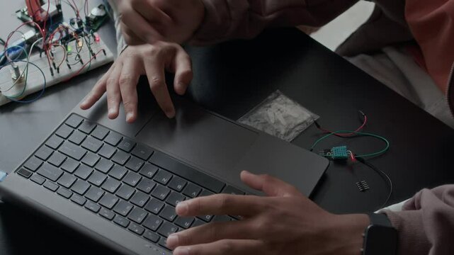 From above shot of two unrecognizable gen z schoolboys using laptop while preparing electronics project together at desk in classroom, working with circuit board details and wires