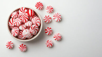 A delightful bowl of red and white striped peppermint candies scattered on a clean surface, perfect for holiday festivities.