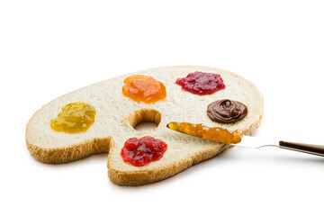 Slice of white bread shaped like a painter's palette with variety of jam spread and knife on white background.