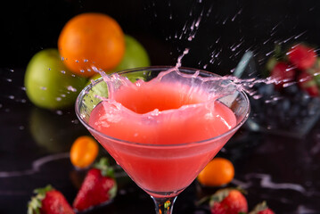 Cocktail glass with fresh fruits, apples, strawberries, kumquats and blueberries making a splash with the liquid flying