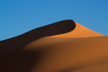 Graphic line of a red dune creating strong contrasts between light and shadow on the background of...