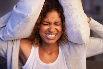 Angry student girl trying to sleep, covering ears with pillows and closing eyes, irritated with...