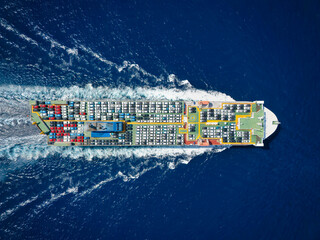 Aerial top down view of a large, industrial car carrier transport ship cruising with peed over the ocean