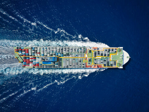 Aerial top down view of a large, industrial car carrier transport ship cruising with peed over the ocean