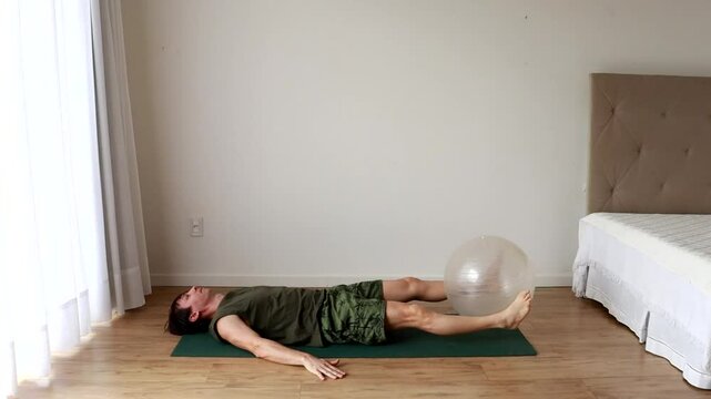 homem faz exercicios fis&iacute;cos e alongamentos com bola de pilates 