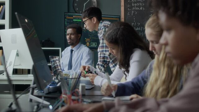 Ethnically diverse teen students having robotics and coding lesson with young Black male teacher in modern classroom