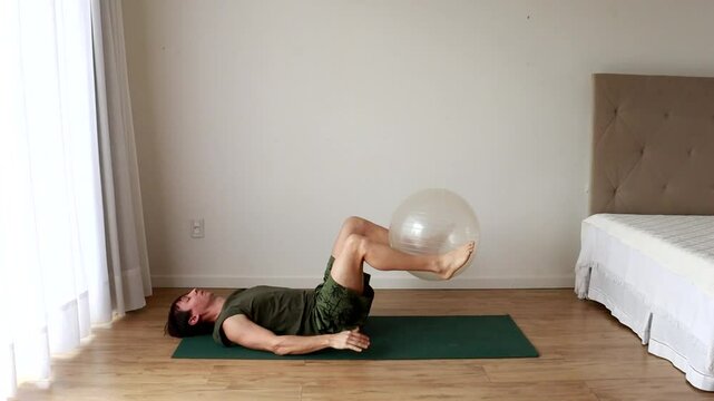 homem faz exercicios fis&iacute;cos e alongamentos com bola de pilates 