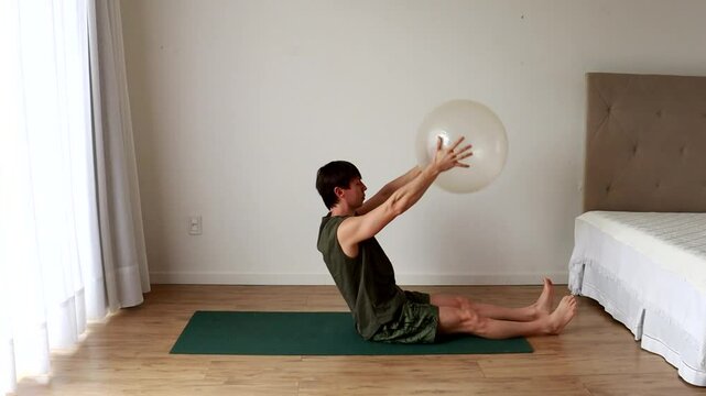 homem faz exercicios fis&iacute;cos e alongamentos com bola de pilates 
