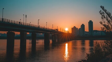 Obraz premium A bridge over a river with a city skyline in the background at sunset.