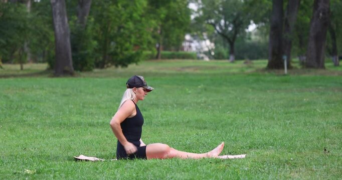 Woman performs Garudasana exercise, eagle pose, leads healthy lifestyle and practices yoga on park lawn, full-length view