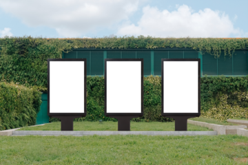 Vertical mock up template: 3 out of home (OOH) advertising billboard posters on grass, against background of lush plant wall of building. Bright day, blue sky with clouds. Transparent png file.