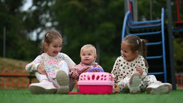 Three sisters sit on the grass at the park, playing with their baby sibling and having fun. A heartwarming video of childhood, happiness and family.
