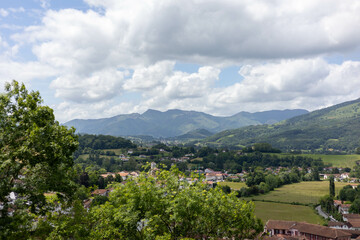 Paysage du Pays basque Français avec un ciel nuageux, une montagne et un petit village entouré de forêt et de champs vert
