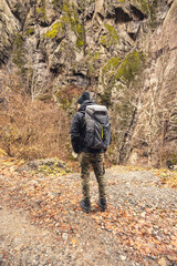 Naklejka premium Amidst golden foliage and towering cliffs, a lone adventurer stands on a trail, captivated by nature's beauty while carrying a sturdy backpack for exploration
