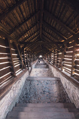 Fototapeta premium A long, illuminated passageway lined with wooden beams stretches toward a distant, glowing light, inviting exploration. The stone steps guide the way down