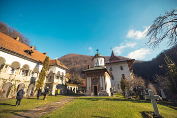 Tourists wander through lush green lawns, admiring the beautiful architecture of the monastery against a stunning blue sky, surrounded by peaceful mountains