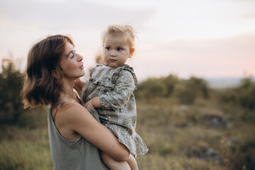Mother Holding Daughter in Scenic Outdoor Landscape at Sunset, Embracing Love and Connection