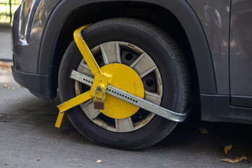 Obraz premium Vehicle immobilized by a bright yellow wheel clamp on a city street during autumn