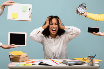 Young African American woman sitting at desk surrounded by hands with alarm clock and gadgets,...