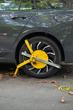 Vehicle immobilized by a bright yellow wheel clamp on a city street during autumn