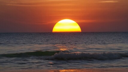 Sunset over the ocean with waves crashing on the shore.